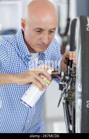 senior man spraying oil to chain from the wheel bike Stock Photo
