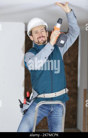 young tradesman using cordless screwdriver on plasterboard ceiling Stock Photo