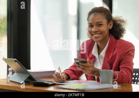 African American businesswoman using calculator and laptop for do math finance on wooden desk in office and business working background, tax Stock Photo