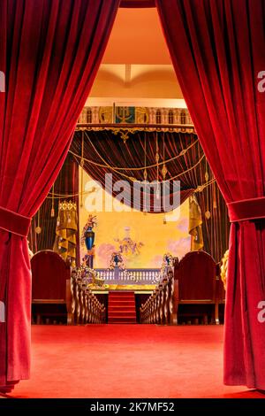 Red velvet curtains that reveal the interior of the theater in the background. Stock Photo