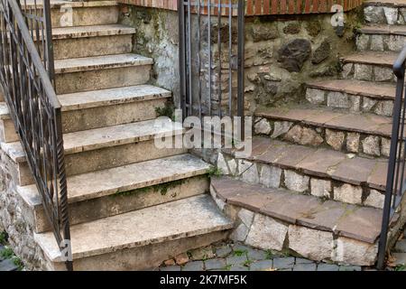 Two stone staircases with metal forged railing and a gate in the corner of old medieval house. Italian old town architectural element. Marble steps Stock Photo