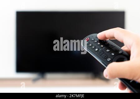 The man with the remote control in hand watching the sports channel and presses the button on the remote control. Remote control in hand closeup. Stock Photo