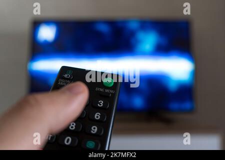 The man with the remote control in hand watching the sports channel and presses the button on the remote control. Remote control in hand closeup. Stock Photo