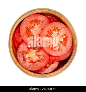 Fresh plum tomato slices, in a wooden bowl, isolated from above. Sliced red ripe oval tomatoes, layered on top of each other. Stock Photo