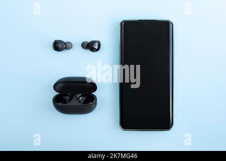 Smartphone and wireless headphones or earbuds with charging case on bright blue background. Music technology trends. top view Stock Photo