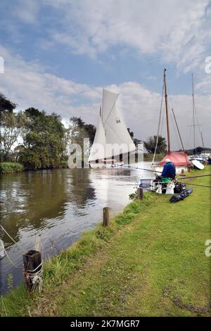 match fisherman and traditional broads sailing boat on river thurne martham norfolk england Stock Photo