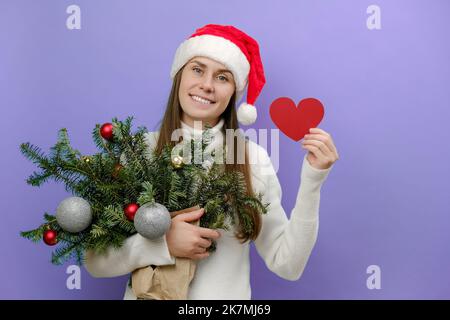 Portrait of charming young girl hold small red heart and handmade green spruce bouquet prepares for Christmas in advance enjoys New Year festival, iso Stock Photo