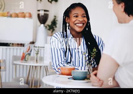 Happy young businesswoman smiling while having a coffee meeting with a colleague in a cafe. Two cheerful businesswomen having a friendly conversation Stock Photo