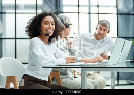 smiling female call center worker accompanied by her team working in the office. Stock Photo