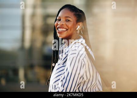 Happy young business woman smiling at the camera while traveling to work in the city. Portrait of a cheerful young business woman listening to music o Stock Photo
