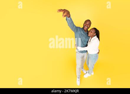 African American Spouses Advertising Something Holding Invisible Object, Yellow Background Stock Photo