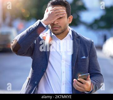 The worst way to end a day. a young businessman experiencing a headache while using his smartphone. Stock Photo
