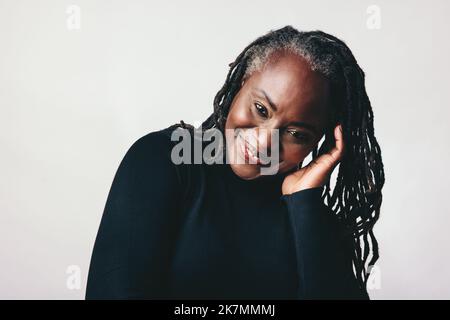 Confident mature woman smiling at the camera while touching her dreadlocks. Happy middle-aged woman embracing her natural hair with pride. Cheerful bl Stock Photo