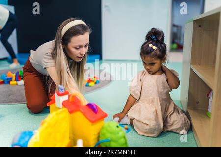 lovely little girl and her teacher having fun at the nursery, toys in the background. High quality photo Stock Photo