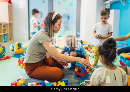 young and beautiful teacher and toddlers playing with building blocks toy at the nursery, full shot. High quality photo Stock Photo