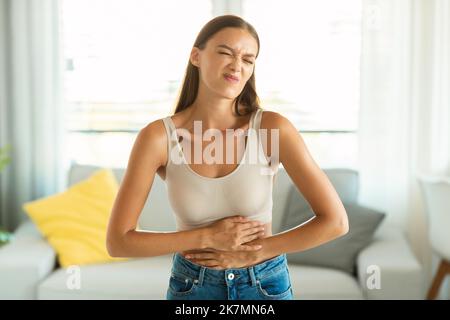 Unhappy Female Suffering From Stomachache Touching Aching Belly At Home Stock Photo