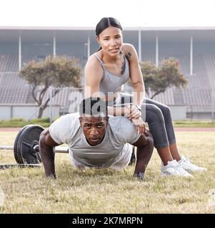We put in the work it takes to stay fit. a young woman sitting on a mans back while he does push-ups. Stock Photo