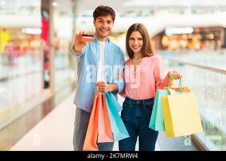 Cheerful Spouses Showing Credit Card Holding Shopper Bags In Mall Stock Photo