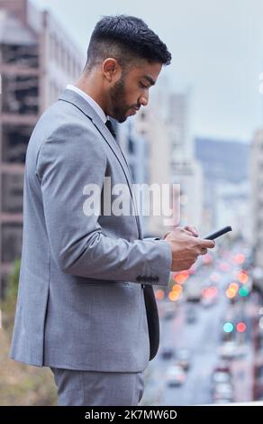 Success waits for no one. a handsome young businessman standing alone and using his cellphone. Stock Photo
