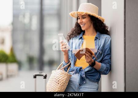 Positive middle eastern woman standing by airport, using smartphone Stock Photo