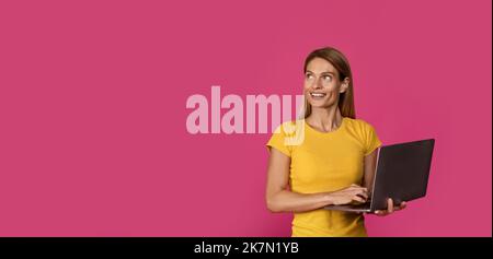 Smiling mature european female with laptop looking at empty space, isolated on purple background Stock Photo