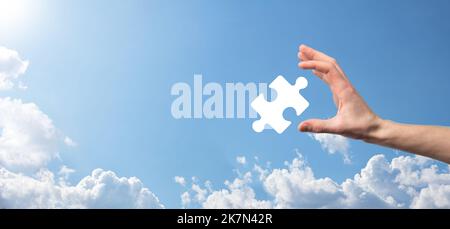 Male hand holding puzzle icon on blue background. pieces representing the merging of two companies or joint venture, partnership, Mergers and acquisit Stock Photo