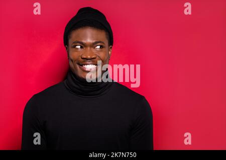 Photo of funny sweet young guy wear black turtleneck headwear looking empty space isolated red color background Stock Photo