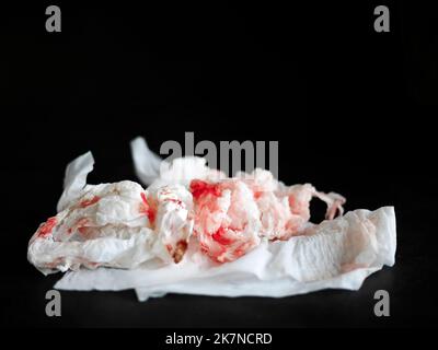 Fresh red blood stained on tissue paper isolated on dark background, used crumpled wipe paper, bleed, copy space Stock Photo