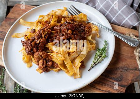 Italian ragout with chicken, tomatoes, onions, garlic, herbs and red wine sauce on a plate with tagliatelle Stock Photo