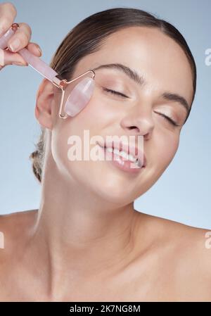 Face it, shes beautiful. Studio shot of an attractive young woman using a face massager against a grey background. Stock Photo