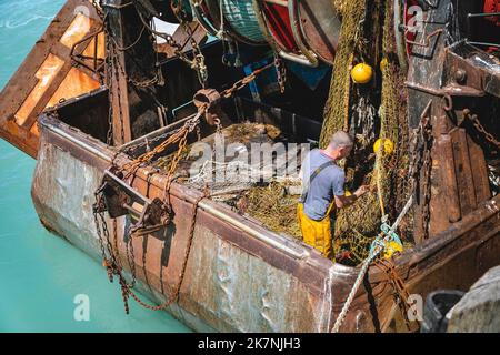 Cancale (Brittany, north western France): trawler alongside the quay. Deep sea fisherman repairing fishing nets Stock Photo