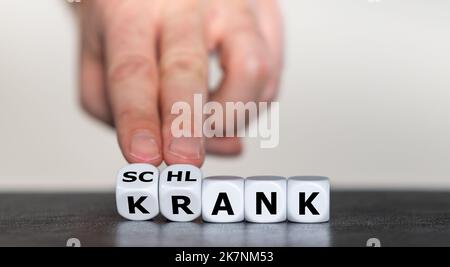 Hand turns dice and changes the German word 'krank' (sick) to 'schlank' (slim). Stock Photo