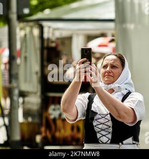 Hannover, Germany, June 11, 2022: Old woman in north german costume with headscarf takes a selfie with her mobile phone Stock Photo