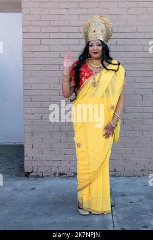 A pretty Hindu woman wearing a yellow sari & crown and dressed as the Goddess Lakshmi. At Diwali 2022 in Queens, New York City. Stock Photo