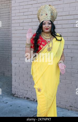A pretty Hindu woman wearing a yellow sari & crown and dressed as the Goddess Lakshmi. At Diwali 2022 in Queens, New York City. Stock Photo