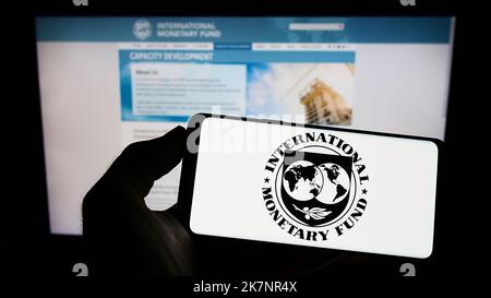 Person holding cellphone with logo of UN agency International Monetary Fund (IMF) on screen in front of webpage. Focus on phone display. Stock Photo