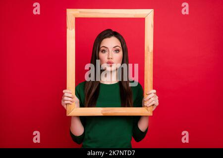 Photo of flirty brunette lady blow kiss in frame wear green shirt isolated on red color background Stock Photo