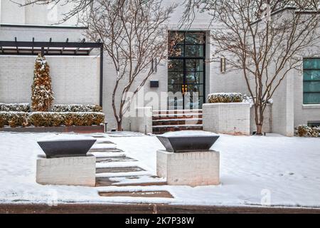Entrance to attractive white brick modern home in snow with glass doors and wall to patio area - front steps and empty flower containers Stock Photo