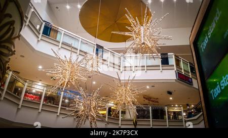Golden holiday decorations hanging from ceiling of multi-story mall shopping center with people walking on different levels and up escalator Stock Photo