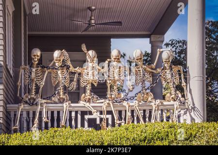 Life sized Skeleton Chain Gang sits on banister of vintage home porch - Halloween decoration Stock Photo