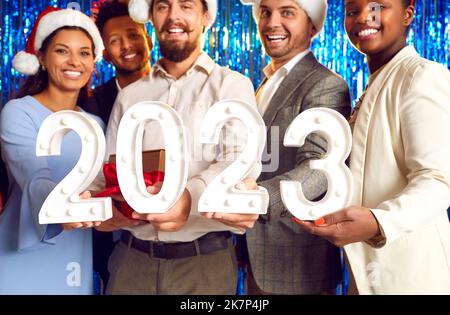 Team of happy joyful diverse people with 2023 digits at corporate New Year party Stock Photo