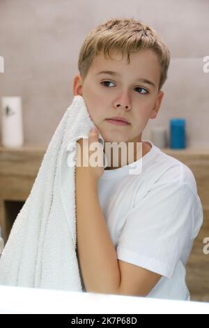 Reflection of schoolboy wiping his face with a towel after washing in bathroom. Stock Photo