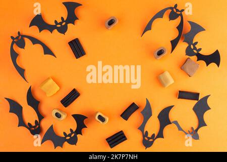 Composition for halloween from bats Cut out of paper and various candies, on an orange background.  Free space in the center Stock Photo