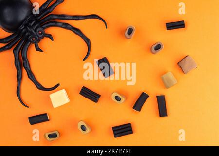 Composition to Halloween from various candies and spiders in the corner of the frame, on an orange background. Stock Photo