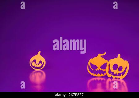 Three angry orange paper-cut pumpkins stand on a purple background.  Halloween concept, lots of empty space Stock Photo