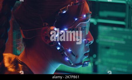 Side view of an Asian girl with futuristic headset and microphone programming using multiple computer screen. Cyperpunk style. Sci-fi background. Stock Photo