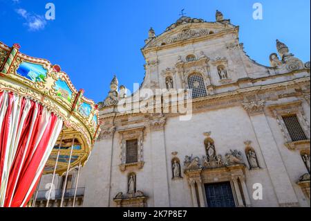 Front of the baroque Church of Saints Peter and Paul the Apostles with a funfair carousel in the foreground in Galatina, Apulia (Puglia), Italy. Stock Photo