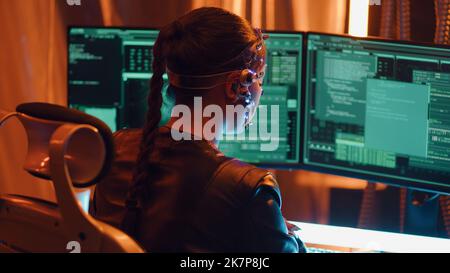 Back view of a Cyberpunk girl types on the keyboard. Multiple computer screen with strings of codes infront of her. Devloping codes for futuristic software. Neon lights in the background. Stock Photo