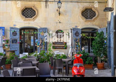 Outdoor seating and red moped in front of restaurant Salumeria Di Turno in Galatina old town, Apulia (Puglia), Italy. Stock Photo