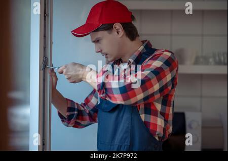 Calm focused serviceman installing the window locking mechanism Stock Photo